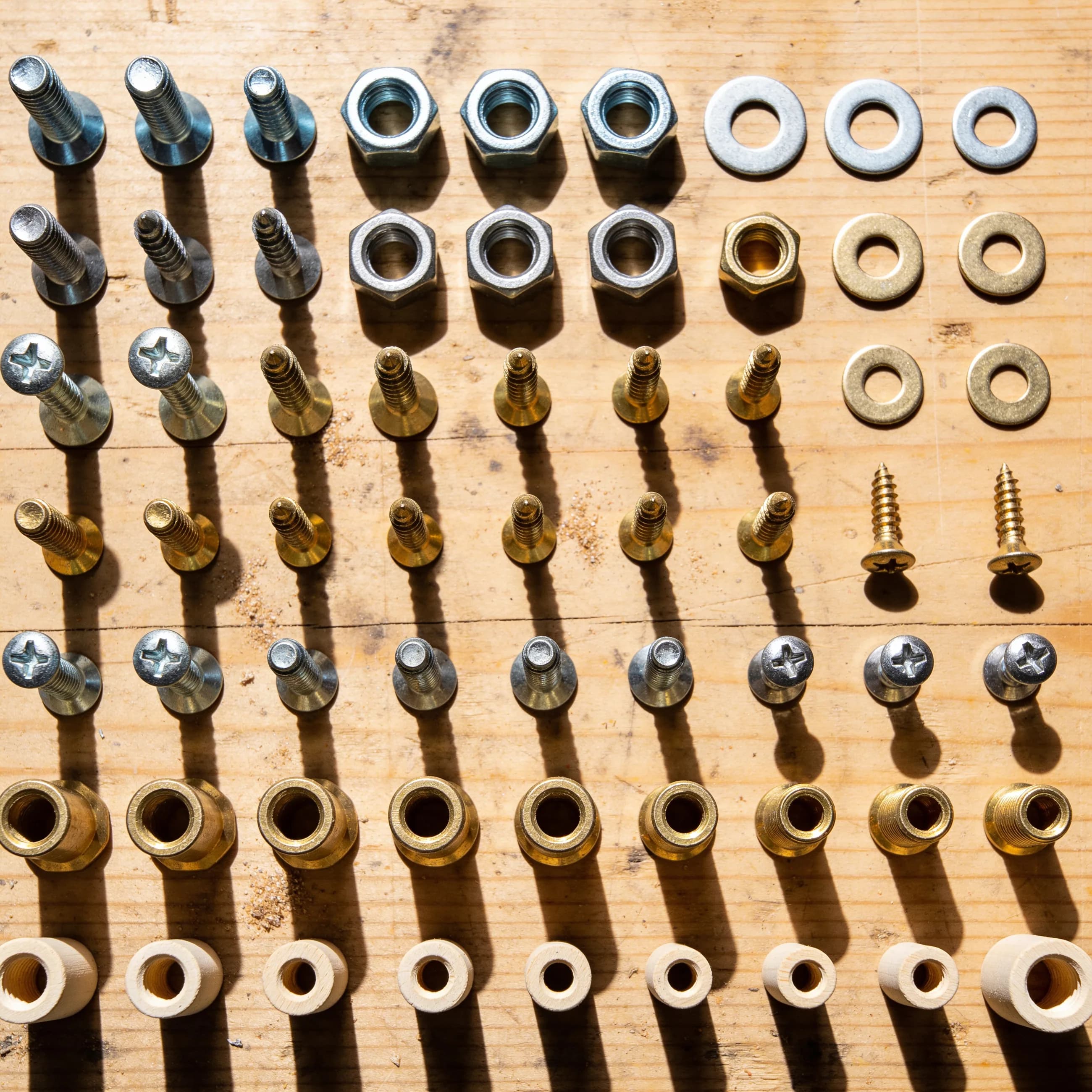 Steel and brass fasteners laid out in sorted rows on a workbench — hex bolts, socket screws, wing nuts and washers.